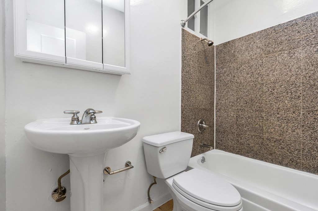 A white sink and toilet in a bathroom with a brown tiled shower.
