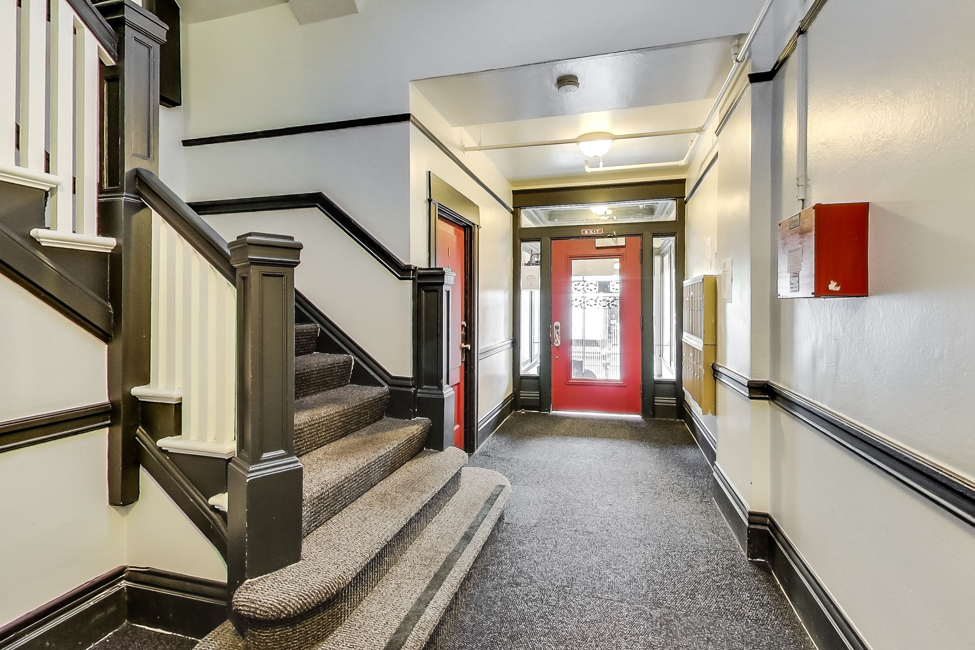 A hallway with a staircase on the left and a red door on the right.