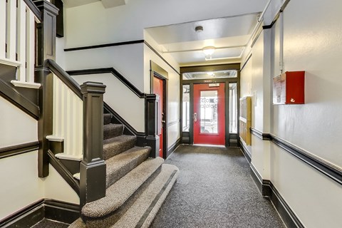 A hallway with a staircase on the left and a red door on the right.