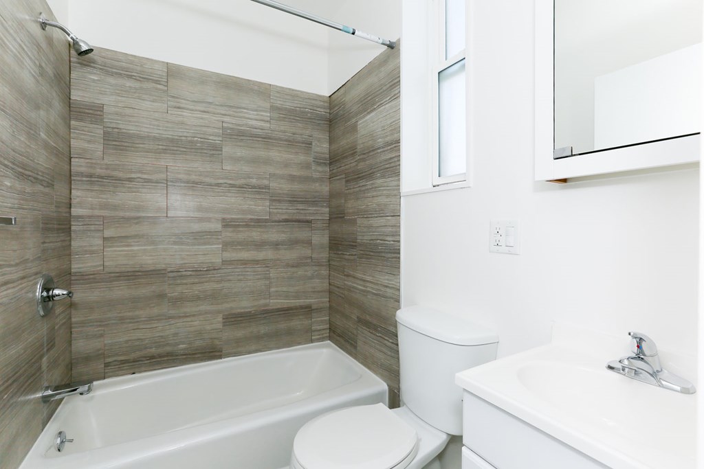 A white toilet sits next to a bathtub in a bathroom with a tiled wall.