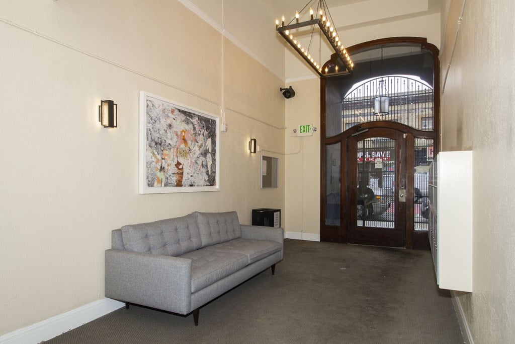 A grey sofa sits in a room with a framed picture on the wall and a door with a sign that says "EXIT" above it.