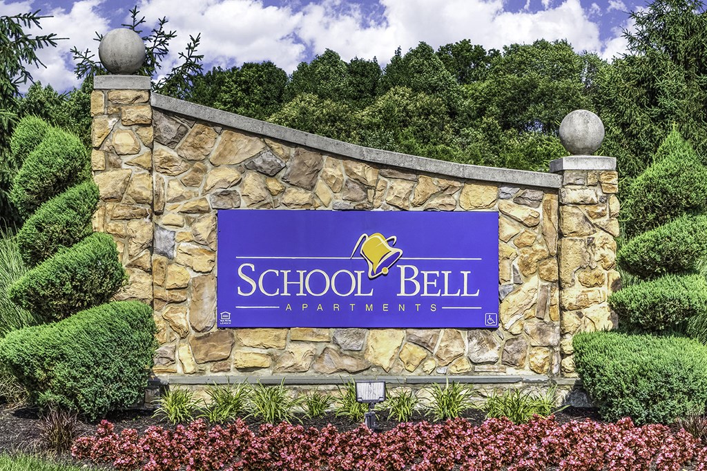 a sign for school bell apartments in front of a stone wall