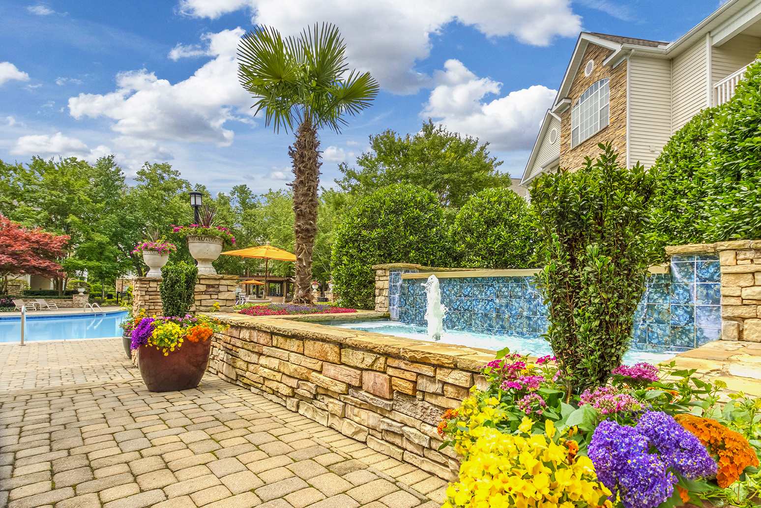 a backyard with a pool and flowers and a stone retaining wall