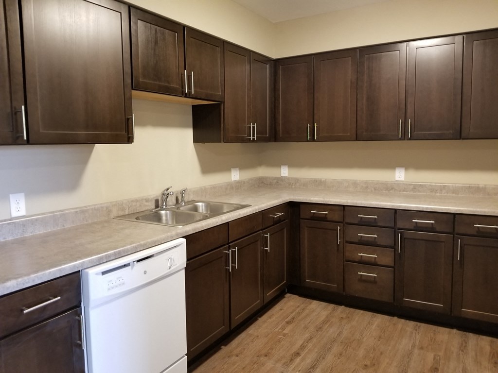an empty kitchen with dark wood cabinets and a white dishwasher and sink