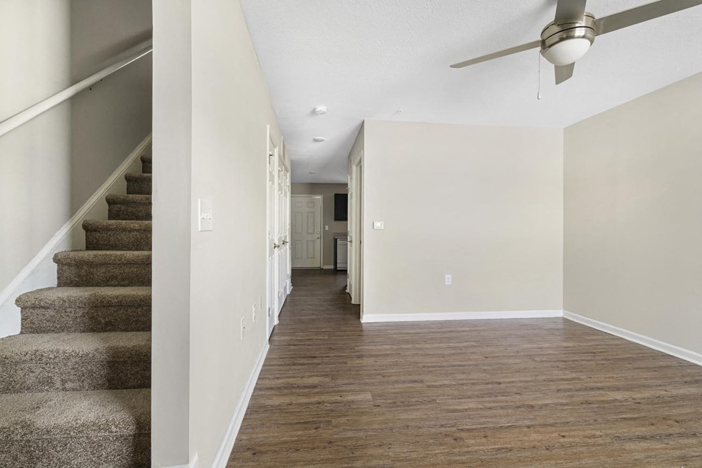 an empty living room with stairs and a ceiling fan