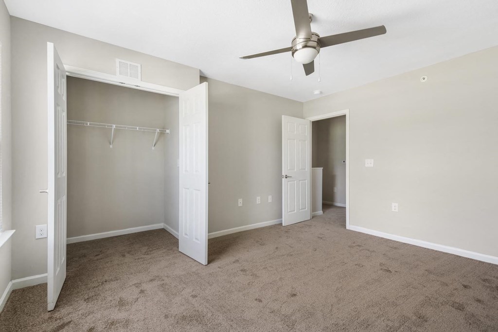 an empty living room with a ceiling fan and a closet