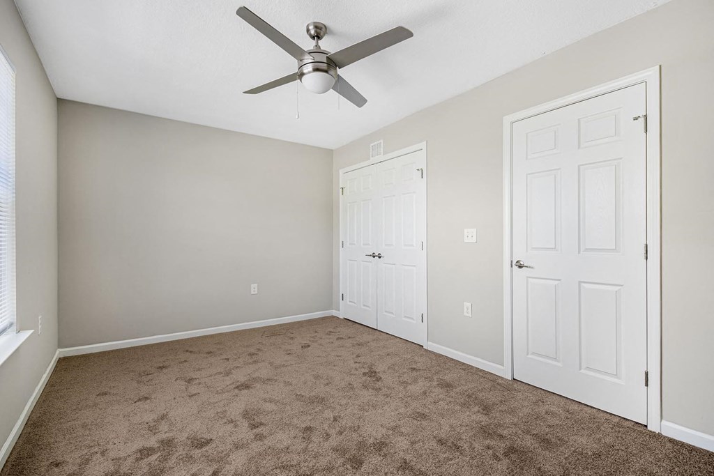 an empty bedroom with a ceiling fan and a closet