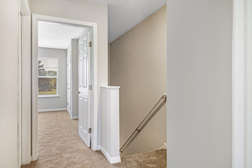 a room with a staircase and a hallway with a door and a window