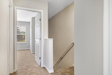 a room with a staircase and a hallway with a door and a window