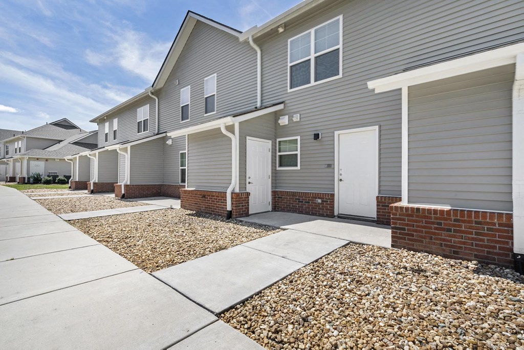 a sidewalk in front of a gray house with white doors