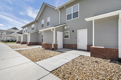 a sidewalk in front of a gray house with white doors