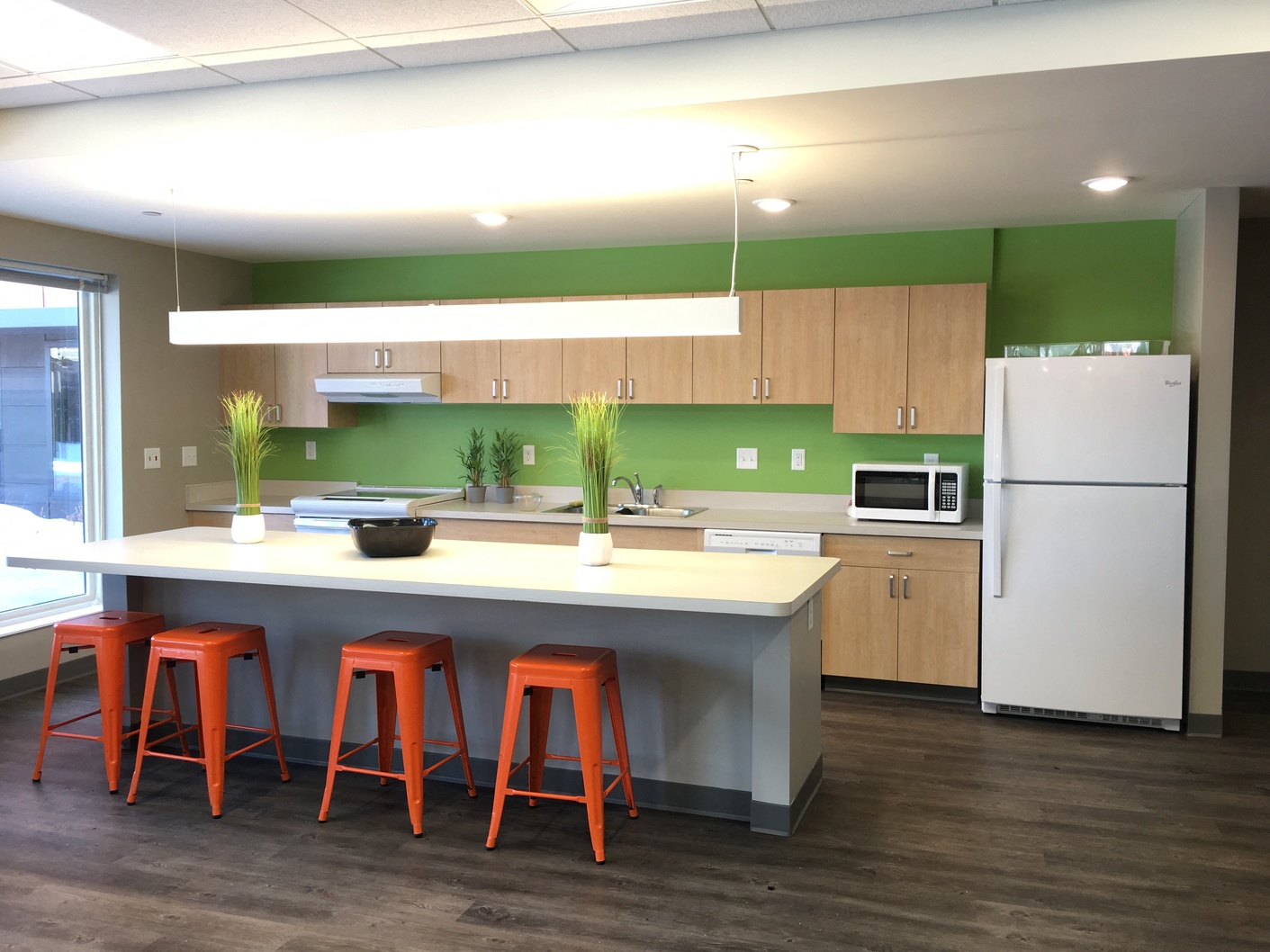 A kitchen with a white refrigerator, orange stools, and a white counter.