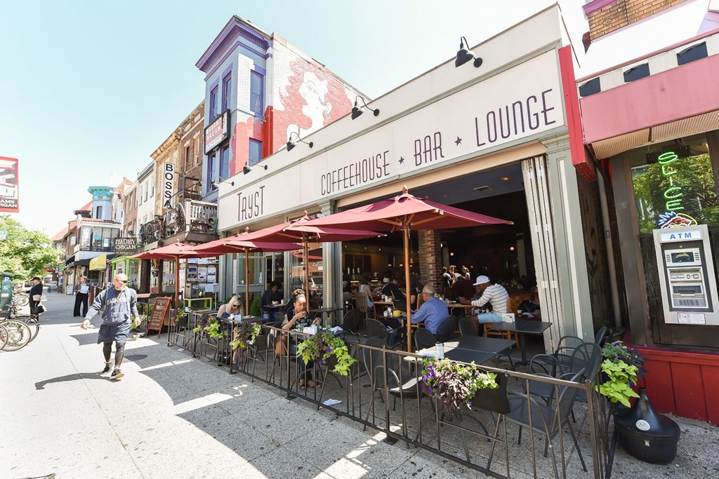 people sitting at tables outside of a restaurant on a sidewalk