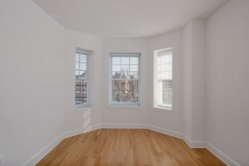 a living room with three windows and a wooden floor