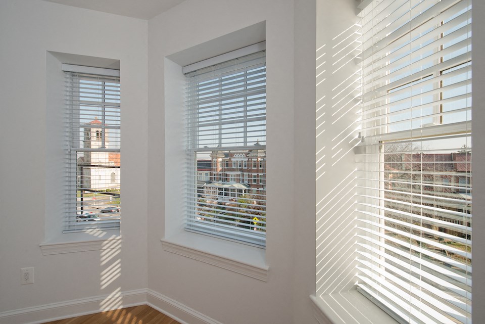 a living room with two windows with blinds and a city view