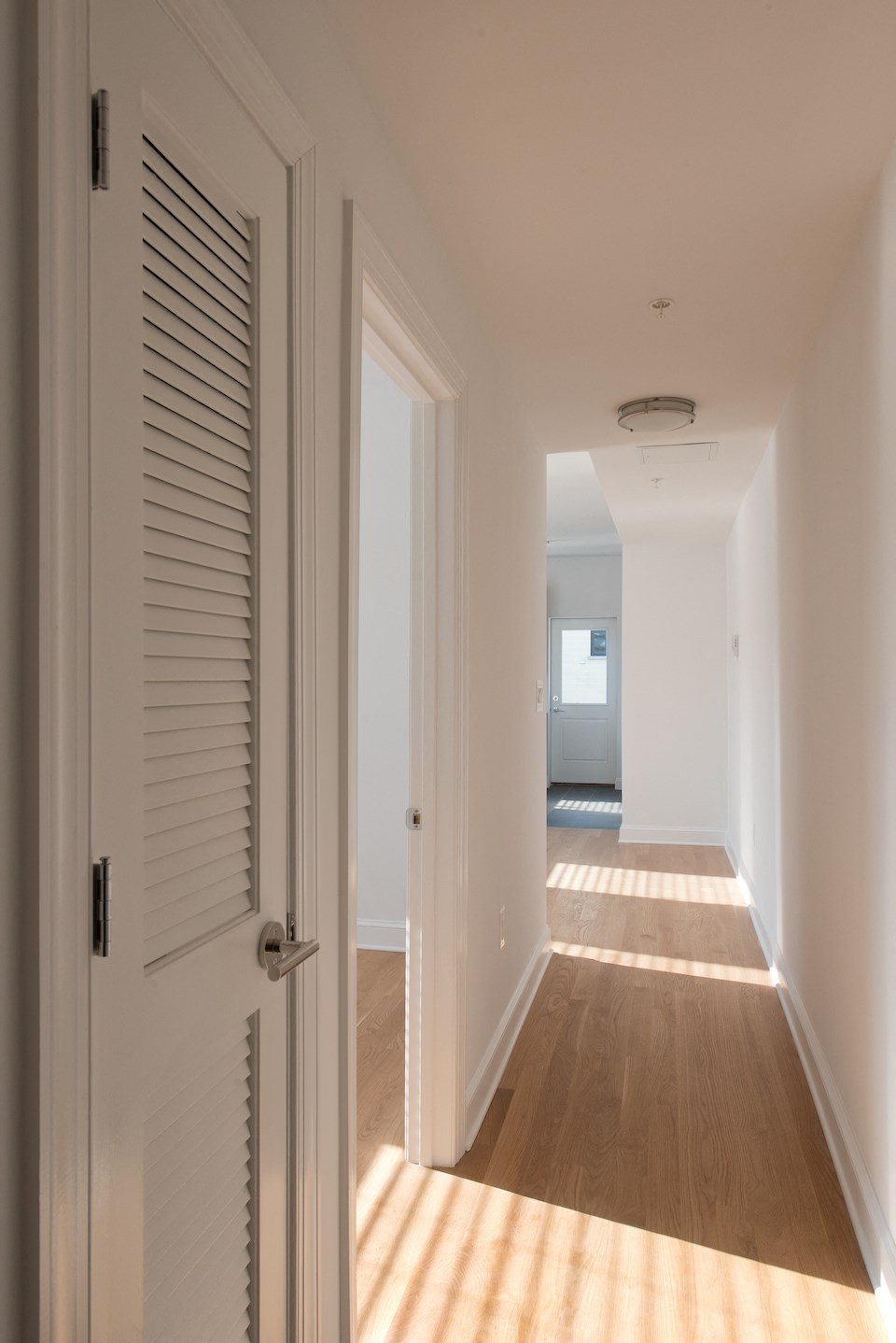 a hallway with white walls and wooden floors and a white door