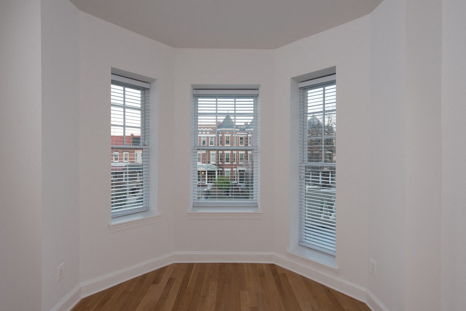 a living room with three windows and a wooden floor