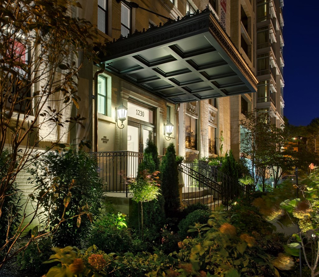 the front of a building at night with a garden in front of it