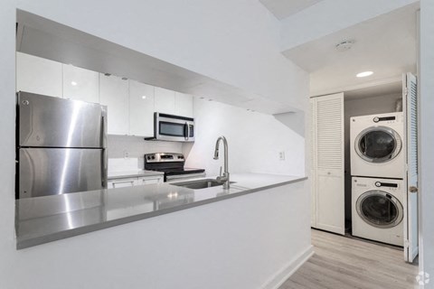 a white kitchen with a washer and dryer and a stainless steel refrigerator