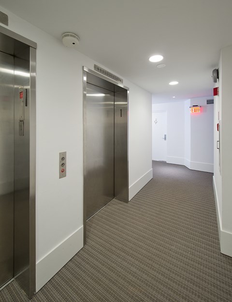 a hallway with stainless steel elevators and white walls
