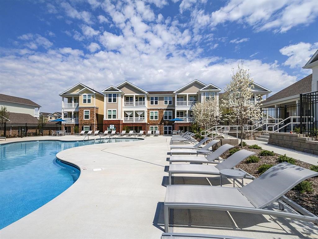 an empty pool with lounge chairs in front of an apartment building