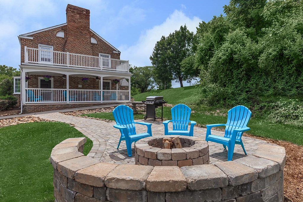 a fire pit with blue chairs and a house in the background