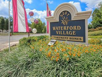 a sign for waterford village with flags and grass and flowers