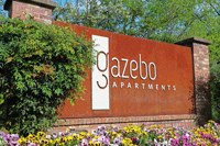 a sign at the gatezo apartments in front of a bush and flowers