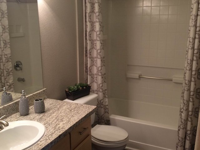 Apartments in Roseville for Rent - Pinnacle at Galleria - Apartment Bathroom With a Mirror and Sink, a Toilet, and a Shower With Tile Walls and a Curtain