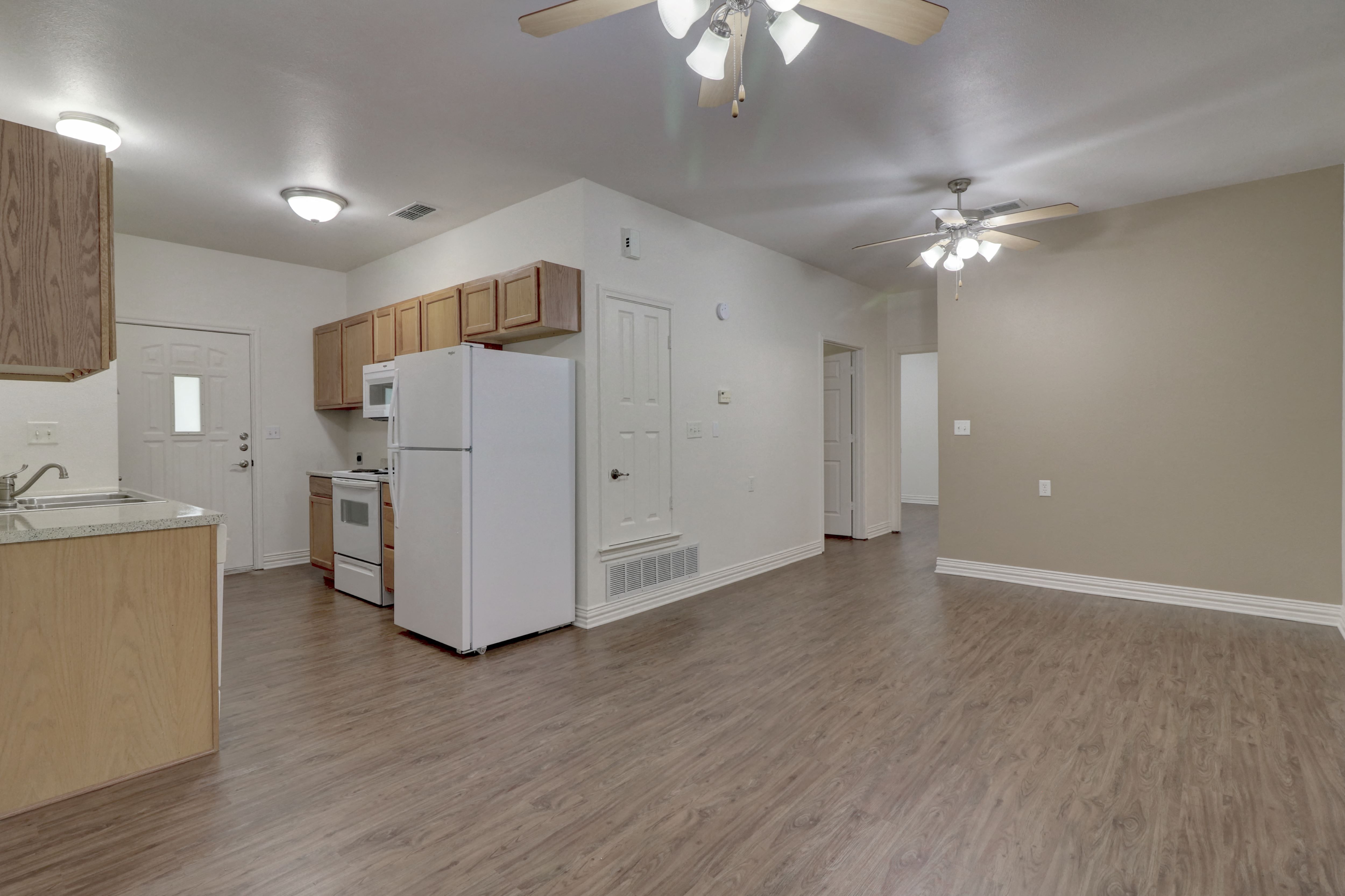 an empty living room and kitchen with a white refrigerator and a ceiling fan