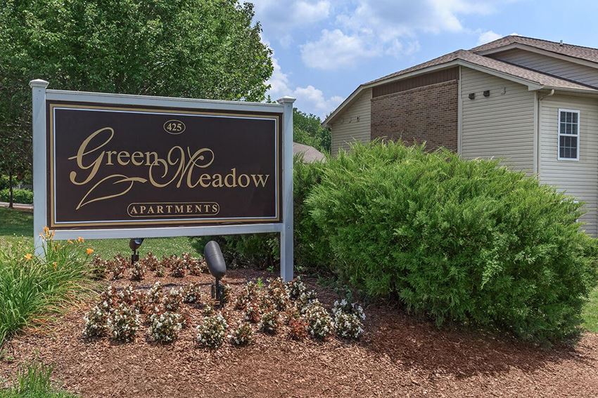 a sign for green meadow apartments in front of a house