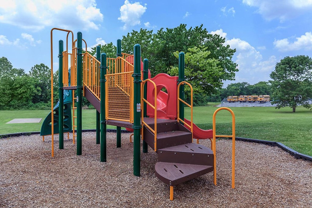 a playground with a slide and chairs in a park