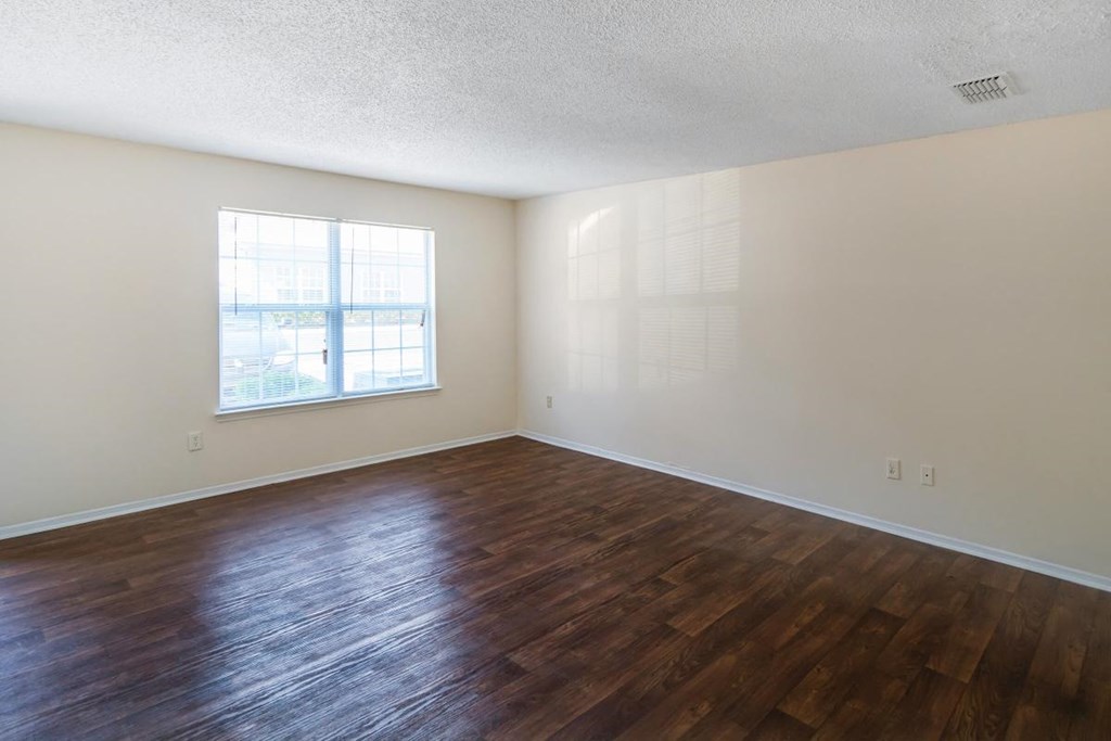 an empty living room with wood flooring and a window