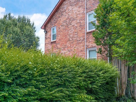 the side of a brick house with trees and bushes
