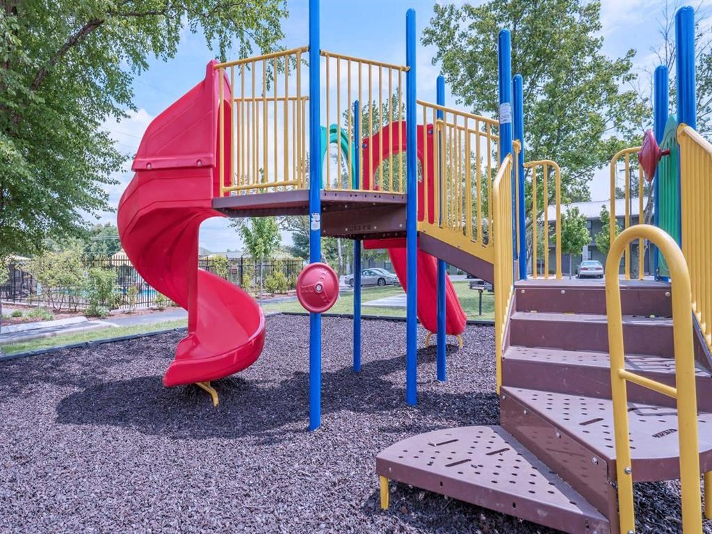 a playground with a red slide and a bench in a park
