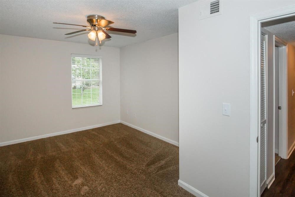 an empty bedroom with a ceiling fan and a window