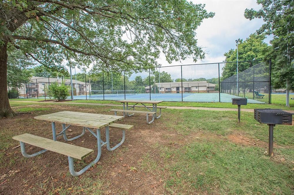 two picnic tables and a grill in front of a tennis court