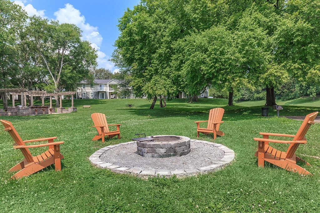 a fire pit in the middle of a lawn with rocking chairs