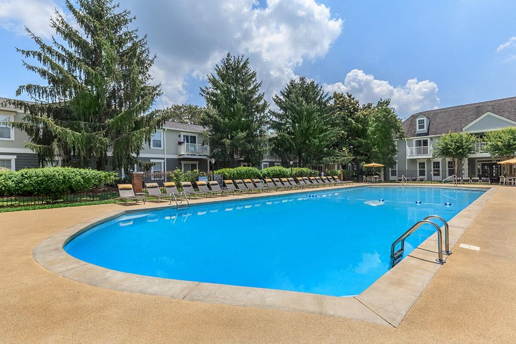 a large swimming pool with chairs around it in front of an apartment building