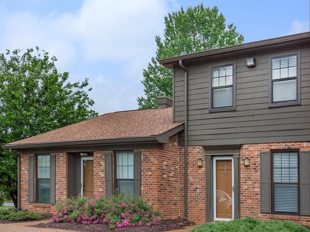 the front of a brick house with bushes and trees