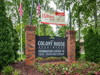 a sign for the colony house apartments entrance with flags and trees