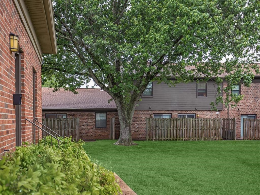 the back yard of a brick house with a tree and a fence