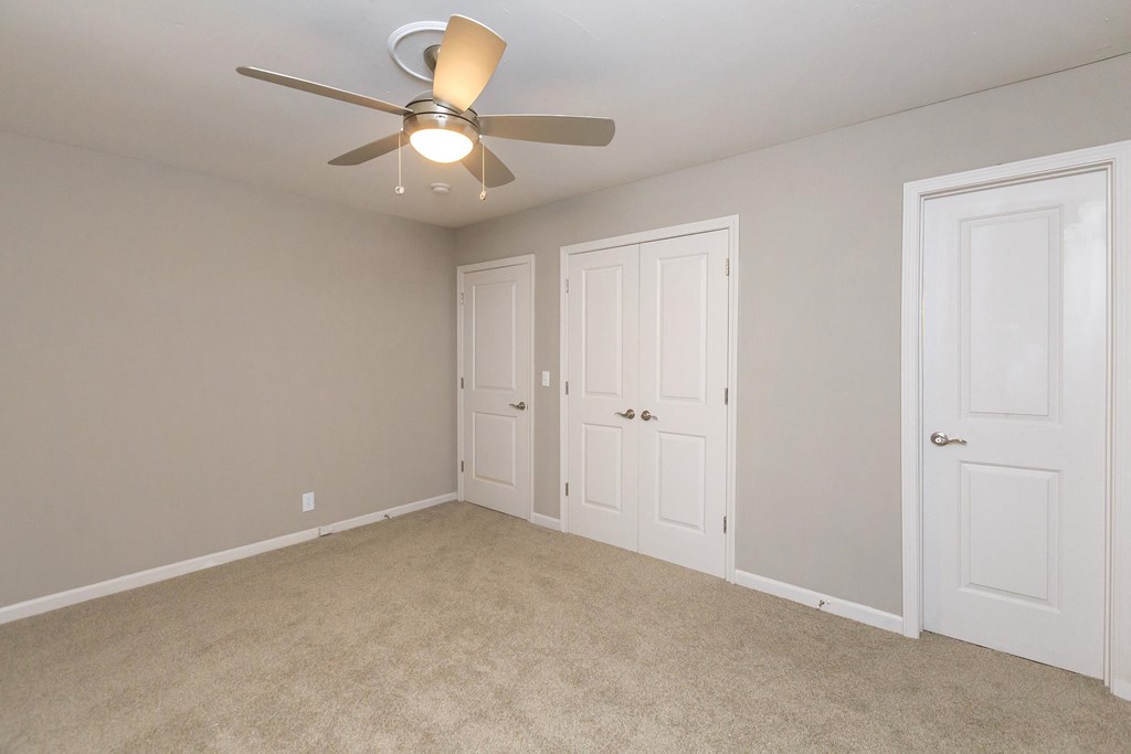 an empty bedroom with a ceiling fan and two doors