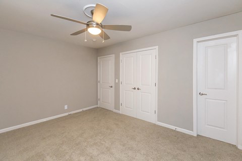an empty bedroom with a ceiling fan and two doors