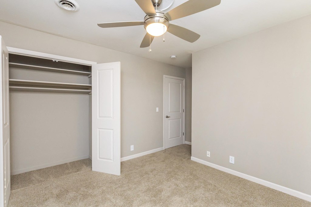 an empty bedroom with a ceiling fan and a closet