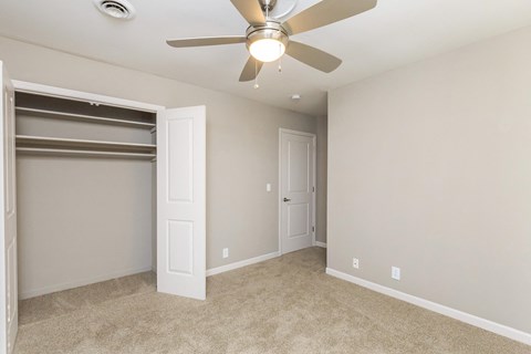 an empty bedroom with a ceiling fan and a closet