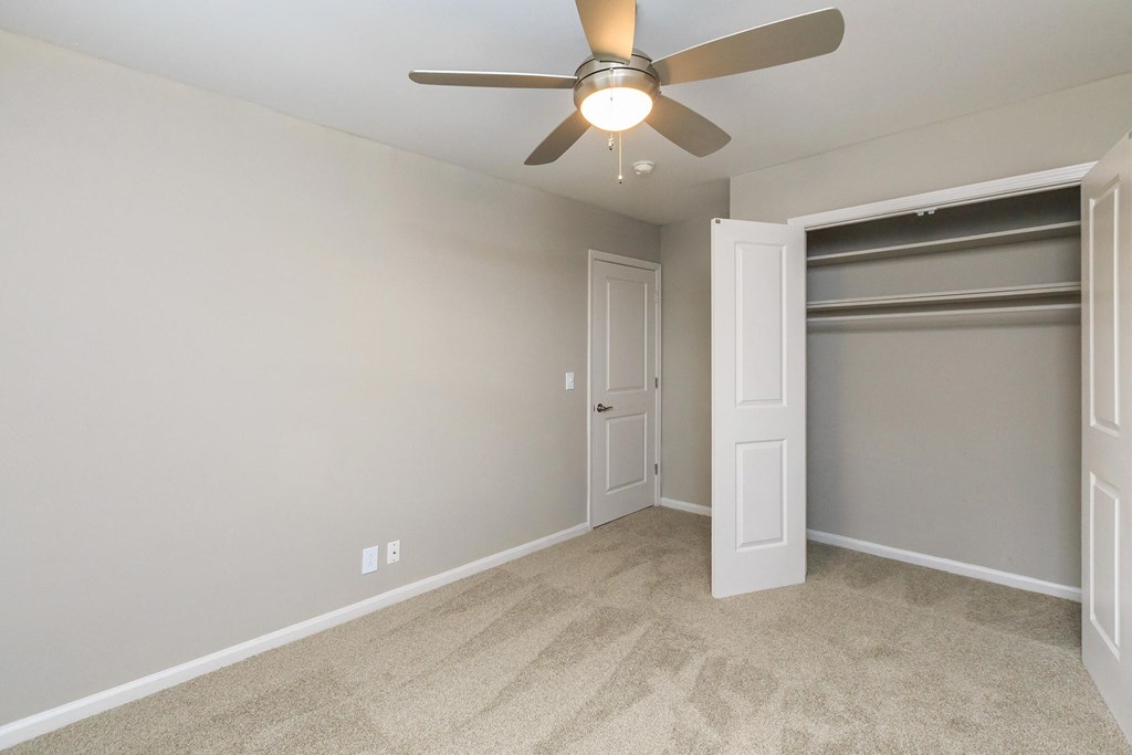 an empty bedroom with a ceiling fan and a closet