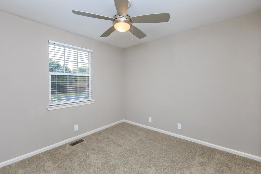 an empty bedroom with a ceiling fan and a window
