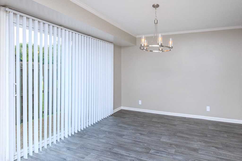 an empty living room with white blinds and a chandelier