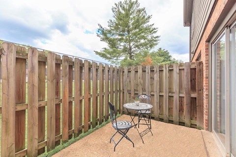 a patio with a table and chairs in front of a fence